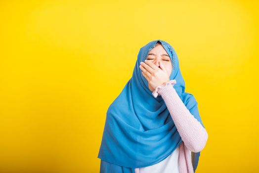 Asian Muslim Arab, Portrait of happy beautiful young woman Islam religious wear veil hijab funny she sleepy yawning wide open mouth hand cover mouth eyes closed studio shot isolated yellow background