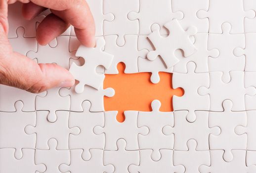 Top view flat lay of hand-holding last piece white paper jigsaw puzzle game last pieces put to place for solve problem complete mission, studio shot on an orange background, quiz calculation concept