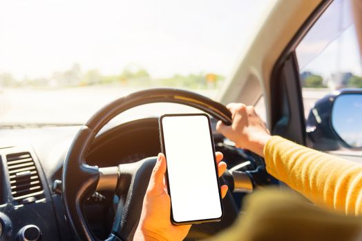 Asian woman inside a car and using a hand holding mobile smartphone blank screen while driving the car in the morning during going to work on highway, Transportation and vehicle concept