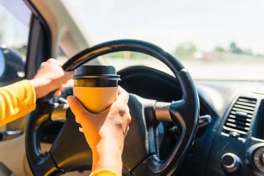 Asian woman drinking hot coffee takeaway cup inside a car and while driving the car in the morning during going to work on highway, Transportation and vehicle concept