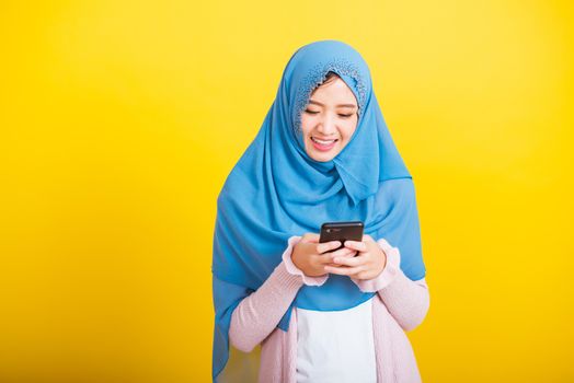 Asian Muslim Arab, Portrait of happy beautiful young woman Islam religious wear veil hijab funny smile she using hold mobile smart phone reading social media isolated on yellow background