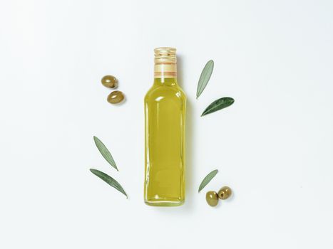 Olive oil glass bottle mock up. Top view of clear glass bottle with olive oil on white background with green olives and fresh green olive tree leaves. Copy space.