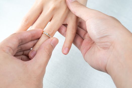Man putting diamond ring on woman hand over white background.