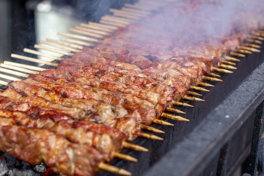 A lot of kebabs in a row on the grill. Kebabs strung on wooden skewers in a street cafe. The process of cooking kebabs with a lot of smoke.