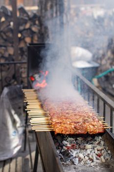 A lot of kebabs in a row on the grill. Kebabs strung on wooden skewers in a street cafe. The process of cooking kebabs with a lot of smoke.