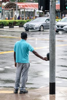 pedestrian pushing button on traffic light pole to get green sign for safely crossing street at intersection, people crossing the street, waiting for flashing lights of walk or don’t walk