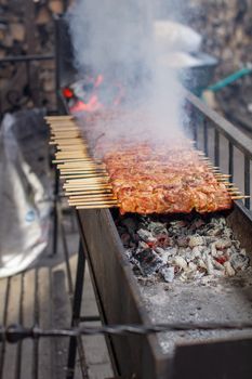 A lot of kebabs in a row on the grill. Kebabs strung on wooden skewers in a street cafe. The process of cooking kebabs with a lot of smoke.