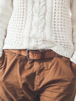 Woman in cable-knit white sweater with Scandinavian patter and brown chinos trousers with leather belt. Casual clothes for snuggle weather. Modern urban fashion.
