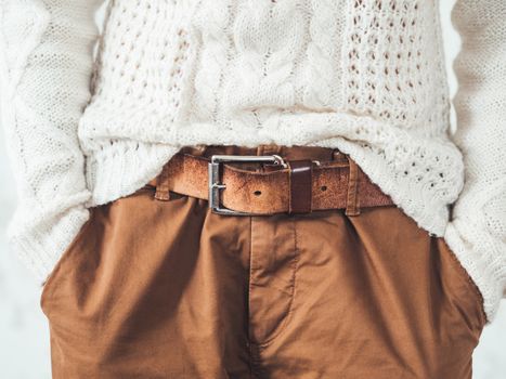 Woman in cable-knit white sweater with Scandinavian pattern and brown chinos trousers with leather belt. Casual clothes for snuggle weather. Modern urban fashion.