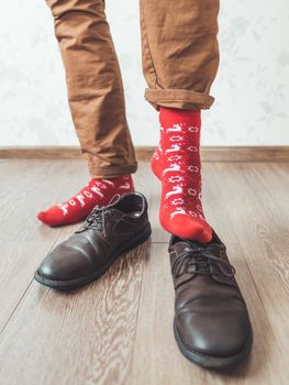 Young man in chinos trousers and bright red socks with reindeers on them is ready to wear suede shoes. Scandinavian pattern. Winter holiday spirit. Casual outfit for New Year and Christmas celebration.