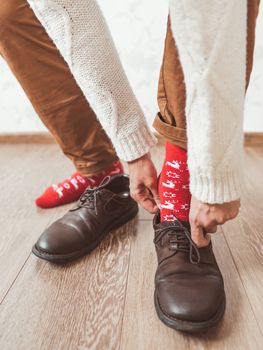 Young man in chinos trousers and bright red socks with reindeers on them is ready to wear suede shoes. Scandinavian pattern. Winter holiday spirit. Casual outfit for New Year and Christmas celebration.