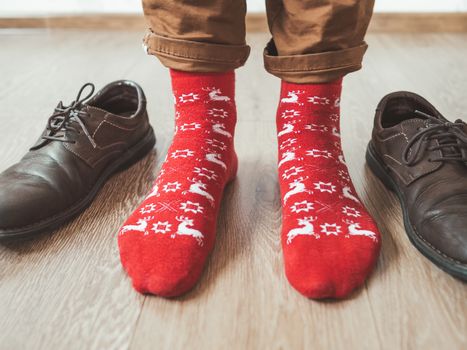 Young man in chinos trousers and bright red socks with reindeers on them is ready to wear sude shoes. Scandinavian pattern. Winter holiday spirit. Casual outfit for New Year and Christmas celebration.