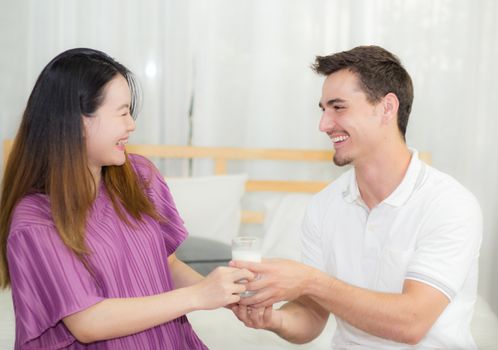 Asian handsome husband takes care about pregnant woman with gives a glass of milk lovely pregnant, family health care concept.