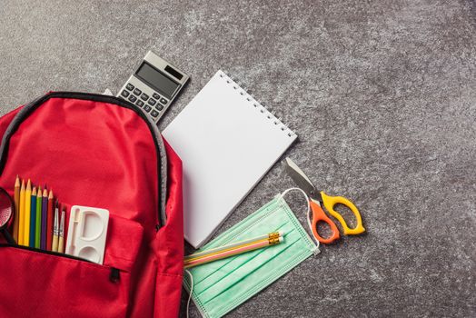 Top view of stylish red school bag backpack on a table desk with face mask protection and stationery, Back to school education new normal during outbreak COVID-19 or coronavirus concept