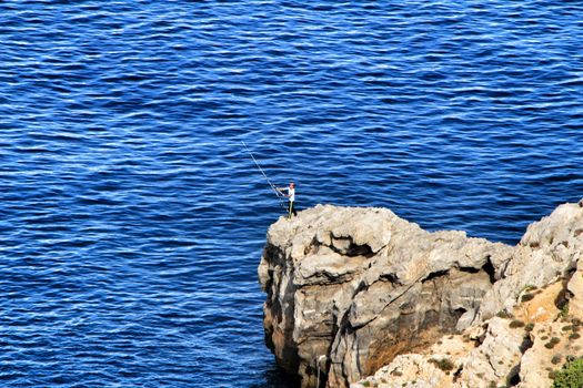 La Azohia, Murcia, Spain- October 2, 2019: Fisherman fishing on the rocks in the evening on La Azohia beach in a sunny day. Cartagena province, Murcia,Spain.