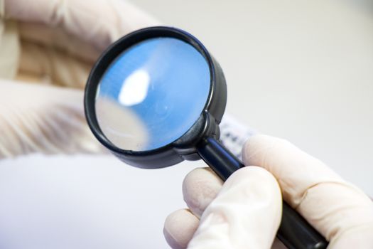 Magnifying glass and human hands with glove, looking and research something. Laboratory situation.