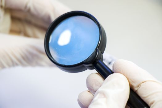 Magnifying glass and human hands with glove, looking and research something. Laboratory situation.