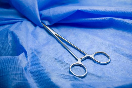 Surgery forceps on the blue background, studio shot. Operation equipment.