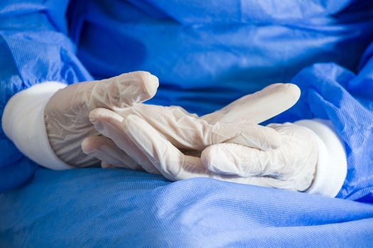Doctors hands with sterile and disinfection white gloves close-up. Surgery and nurse uniform. Blue background.