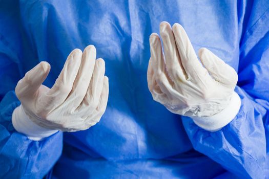 Doctors hands with sterile and disinfection white gloves close-up. Surgery and nurse uniform. Blue background.