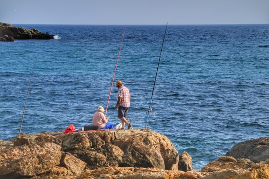 Isla Plana, Murcia, Spain- October 2, 2019: Fisherman and his wife fishing on the rocks in the evening on Isla Plana beach in a sunny day. Cartagena province, Murcia,Spain.