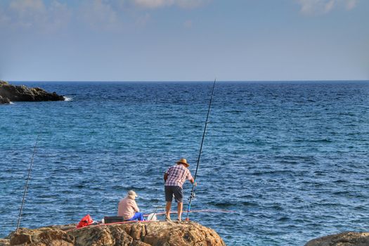 Isla Plana, Murcia, Spain- October 2, 2019: Fisherman and his wife fishing on the rocks in the evening on Isla Plana beach in a sunny day. Cartagena province, Murcia,Spain.