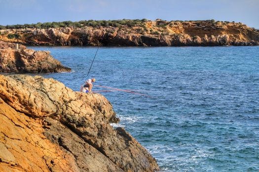 Isla Plana, Murcia, Spain- October 2, 2019: Fisherman and his wife fishing on the rocks in the evening on Isla Plana beach in a sunny day. Cartagena province, Murcia,Spain.
