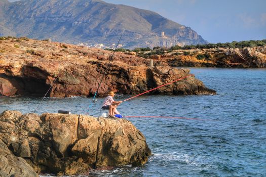 Isla Plana, Murcia, Spain- October 2, 2019: Fisherman and his wife fishing on the rocks in the evening on Isla Plana beach in a sunny day. Cartagena province, Murcia,Spain.