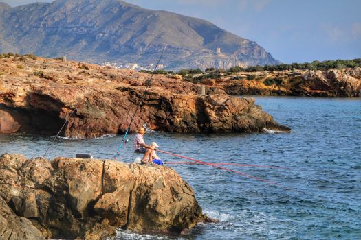 Isla Plana, Murcia, Spain- October 2, 2019: Fisherman and his wife fishing on the rocks in the evening on Isla Plana beach in a sunny day. Cartagena province, Murcia,Spain.