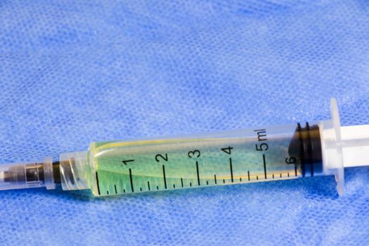 Medical needle on the sterile table with liquid vaccine, yellow vaccine for viruses. Vaccination and antibiotics. Studio shoot.