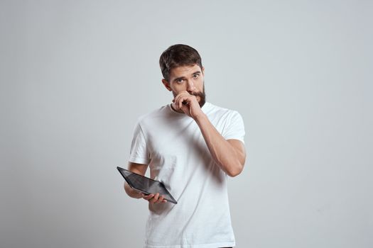 A man in a white T-shirt with a tablet in his hands emotions technology light background. High quality photo