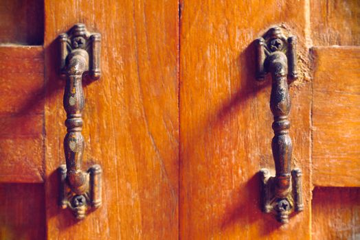 The vintage door handle on an old wooden door background and lighting and shadow in the morning. Closeup and copy space on the centred. The concept of art and architecture in vintage style.