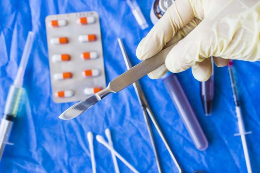 Hand with glove holding surgery blade, drugs, ampule,needle and blood tube on the background