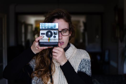 Caucasian girl with dark blond hair with an old automatic printing polaroid camera.