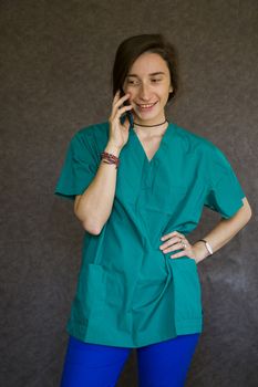 Woman portrait in medical nurse and doctors uniform on the gray background, woman talking on the mobile phone