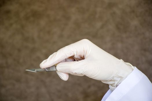 Surgery knife in doctors hand. Operation equipment, hand, glove, and blade on the gray background.