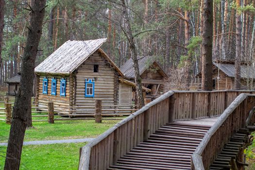 Wooden house with a manor house in the forest. The house has painted Windows. A wooden bridge leads to the house across the river. 