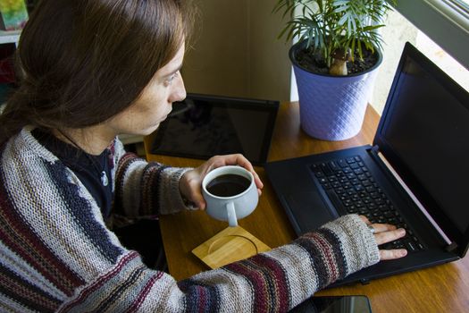 Woman working with notebook in workplace, digital tablet, mobile phone, coffee and plants in workspace, home working