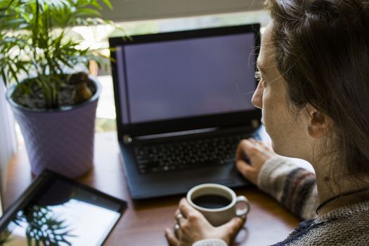 Woman working in office with digital tablet and notebook, writing and typing on the device