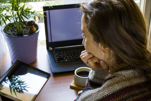 Woman working in office with digital tablet and notebook, writing and typing on the device