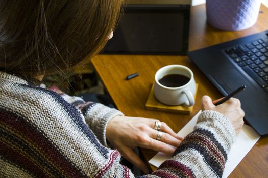 Woman working with notebook in workplace, digital tablet, mobile phone, coffee and plants in workspace, home working