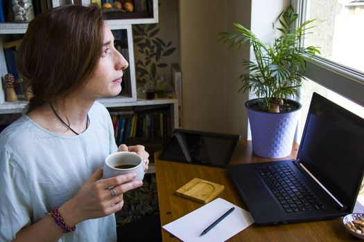 Woman working in office with digital tablet and notebook, looking at the window