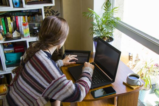 Tbilisi, Georgia - October 09, 2020: Woman working with notebook in workplace, digital tablet, mobile phone, coffee and plants in workspace, home working