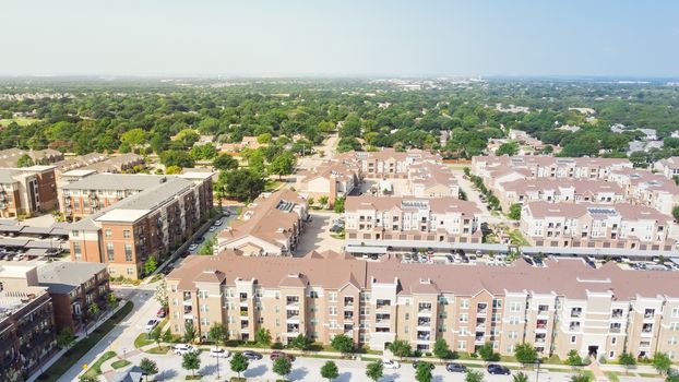 Flyover brand new multistory apartment complex with covered parking lots and suburban residential area in background. Master-planned community and census-designated sprawl in Flower Mound, TX