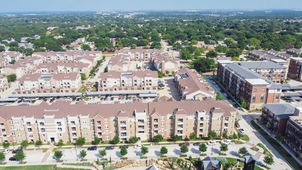 Flyover brand new multistory apartment complex with covered parking lots and suburban residential area in background. Master-planned community and census-designated sprawl in Flower Mound, TX