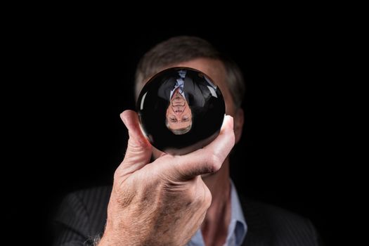 Senior caucasian hand holding glass sphere with upside down reflection of head. Concept for fear of change, new reality or world upside down