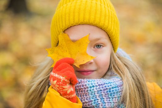 Little girl with blond hair in autumn background in yellow clothing