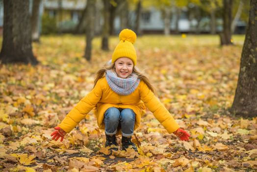 Little girl with blond hair in autumn background in yellow clothing