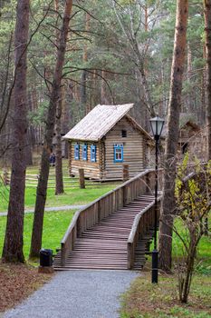 Wooden house with a manor house in the forest. The house has painted Windows. A wooden bridge leads to the house across the river. 