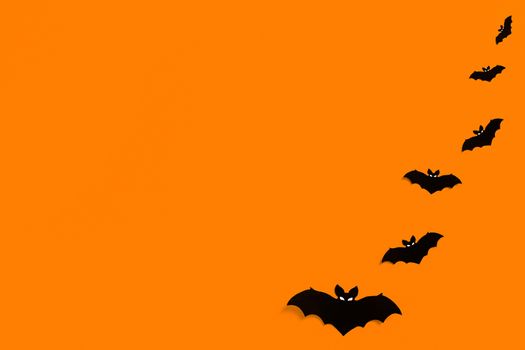 silhouettes of black paper bats on an orange background forming a frame, a flock of black bats on an orange background, Halloween concept, copy space. Flat lay for your design.